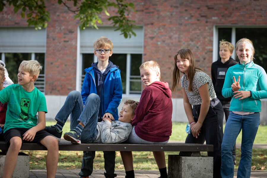 Fünftklässler albern in der Pause gemeinsam auf einer Bank vor dem Schulgebäude herum