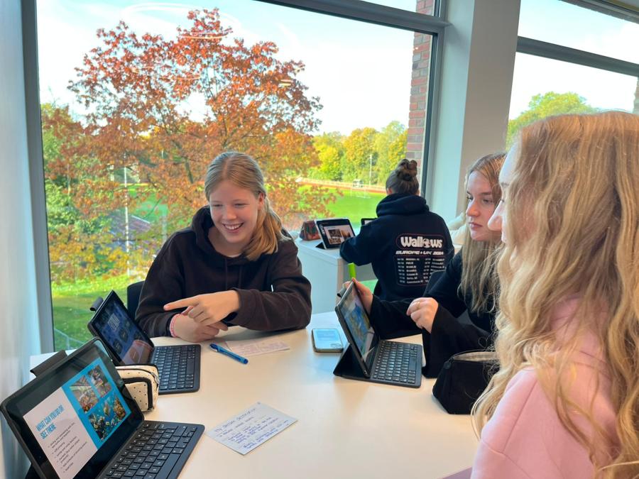 Schülerinnen arbeiten mit iPads an einem Tisch vor großen Fenstern