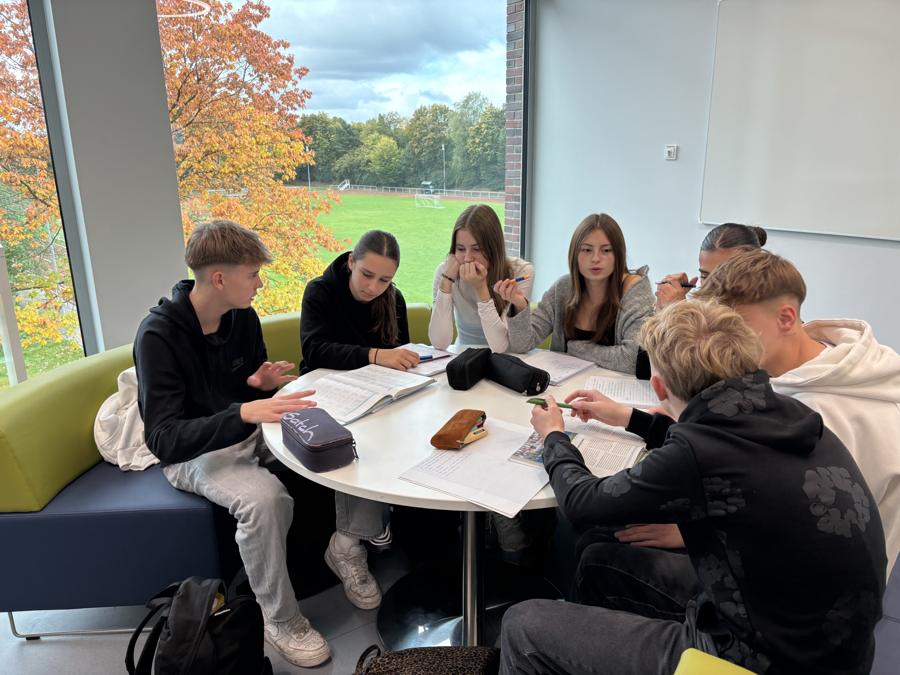 Schülerinnen und Schüler arbeiten gemeinsam an einem runden Tisch im Neubau